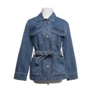 Blå jeansjacka med bälte från mango - Snygg blå jeansjacka från mango i klassisk modell med krage, stora fickor och knappar framtill. Jackan har ett matchande bälte i midjan för extra stilpoäng och långärmade ärmar. Perfekt för dig som gillar en chill och trendig look. Köpt ifrån sellpy men inga defekter, köpt för 600 och säljer för 450.