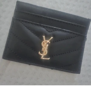 Svart quiltad plånbok i skinn - Stilren svart plånbok i quiltat skinn med guldigt framtill. Smidig och snygg att ha med sig, perfekt för kort och sedlar. Klassisk design med lyxig känsla och flera fack för enkel organisering.