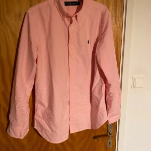 Rosa skjorta från Ralph Lauren S - Snygg rosa skjorta från Ralph Lauren i storlek S. Klassisk button-down med lång ärm och broderad marinblå logga på bröstet. Skjortan är tillverkad i mjuk bomull. Knappt använd men säljer då den är för liten. Kan tänka mig att gå ner i pris vid snabb affär