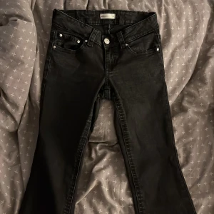 Svarta bootcut jeans från Perfect Jeans - Svarta jeans från Perfect Jeans i storlek 36 med bootcut. Klassisk femficksmodell med silverfärgade knappar och detaljerade bakfickor med lock. Jeansen har normal passform och är tillverkade i ett mjukt jeansmaterial som sitter snyggt och bekvämt.
