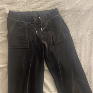 Svarta mjukisbyxor Juicy Couture S - Svarta mjukisbyxor från Juicy Couture i storlek S. Byxorna har bred resår i midjan med snörning, stora fickor fram och bak med silverfärgade knappar, samt en mjuk och glansig sammetstextur. Perfekt för chill dagar och har en klassisk Juicy Couture-logga på fickan pris kan diskuteras💕.