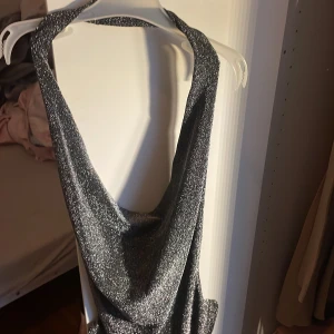 Glittrig silver halterneck topp från TW - Säljer en glittrig silverfärgad halterneck topp body från TW i storlek XS. Toppen har en snygg draperad front och är ärmlös med öppen rygg. Perfekt för att sticka ut med metallic-look och coolt fall. Materialet är syntet med mycket stretch och glittereffekt.