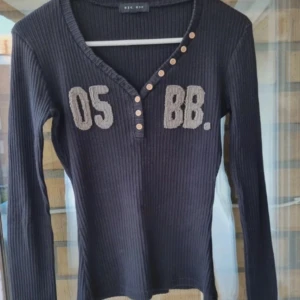 Svart ribbad långärmad tröja - Svart ribbad långärmad tröja med gråa broderade detaljer framtill. 