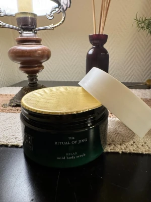 Ritual of Jing mild body scrub - En lyxig body scrub från Rituals, Ritual of Jing-serien. Kommer i en mörkgrön rund plastburk med vitt lock och guldfärgat skydd under locket. Mild formula som exfolierar huden och ger en avslappnande känsla.
