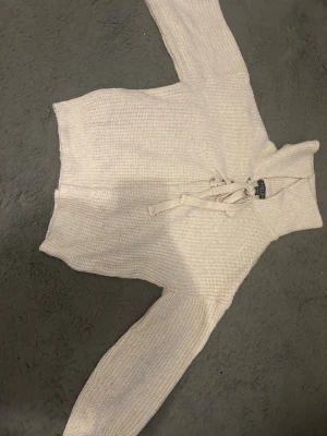 Beige stickad tröja med snörning - Säljer en beige stickad tröja från Amisu med hög krage och snygg snörning framtill. Tröjan har långa ärmar och är gjord i ett grovstickat material som känns både chill och trendigt. Perfekt för dig som gillar detaljer och vill ha något som sticker ut lite extra.