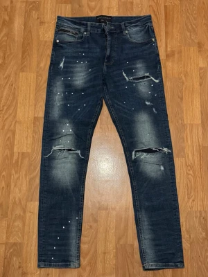 Supply & demand jeans  - Snygga mörkblå jeans från Super X Brand med coola slitningar och pärldetaljer på framsidan. Jeansen har klassisk femficksdesign och en smal passform som sitter riktigt bra. Perfekt för dig som gillar en edgy streetstil.