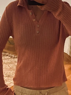 Rosa ribbad tröja med knappar 🎀🎀 - Säljer en rosa ribbad pikétröja med klassisk krage och fyra snygga knappar framtill. Tröjan är långärmad och har en slim passform som sitter snyggt på kroppen. Materialet är stickat och mjukt, perfekt för både vår och höst. Fräsch och trendig färg som lyfter din outfit.