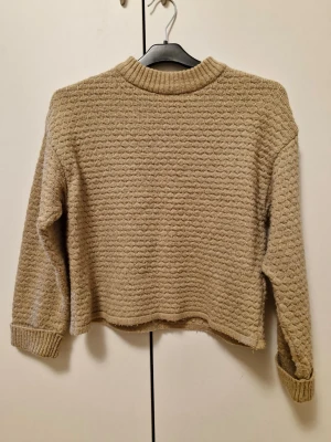 (Barnkläder) Beige stickad tröja från Zara - Mysig beige stickad tröja från Zara med strukturmönster och ribbade muddar vid hals, ärmslut och nederkant. Storleken är 140 cm. Perfekt för kyliga dagar och enkel att matcha med jeans eller kjol.