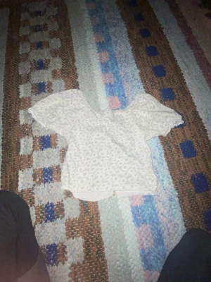 Vit blommig croppad blus - Säljer en söt vit blus med blommigt mönster och croppad passform. Toppen har korta ärmar och en lätt rynkad kant vid ärmslut och nederkant. Perfekt för sommarens alla häng och picknickar. Superfin att matcha med jeans eller kjol!