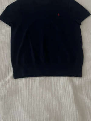 Mörkblå topp från Polo Ralph Lauren - Klassisk mörkblå topp från Polo Ralph Lauren med korta ärmar och rund halsringning. Toppen har en liten röd broderad logga på bröstet och är gjord i mjuk bomull. Enkel och stilren modell som passar till mycket.