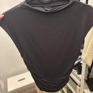 Svart ärmlös topp från Weekday - Säljer en stilren svart topp från Weekday. Modellen är ärmlös med rund hals och har en tight passform som framhäver siluetten. Materialet är mjukt och stretchigt, perfekt för att matcha med jeans eller kjol. Enkelt och snyggt plagg för din garderob.