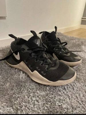 Svarta Nike HyperShift sneakers - Nike HyperShift sneakers i svart med vita detaljer och snörning. Ovandelen är i textil och syntet, med en rund tå och platt sula i ljusbeige. Snyggt camouflagemönster på sidorna och tydliga Nike-loggor. Perfekta för träning eller sport.