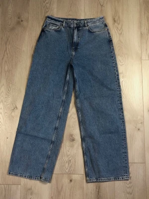 Blå baggy jeans  - Baggy jeans från Never Denim med klassisk femficksdesign och medelhög midja. Jeansen har breda ben och en cool vintage tvätt. Materialet är robust denim i bomull och passformen är loose för en avslappnad stil. Knappt använda. 
