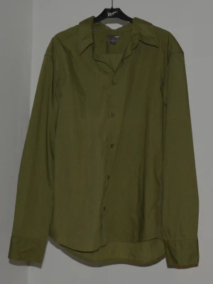 Olivgrön skjorta från H&M (XL) - Olivgrön skjorta från H&M i storlek XL. Klassisk krage, långärmad och med knappar framtill. Skjortan har en loose passform.