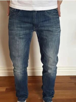 Replay Anbass jeans blå slim fit - Snygga blå Replay Anbass jeans med slim fit och klassisk femficksdesign. Jeansen har en mörk tvätt med lätt slitna detaljer och tydliga sömmar. Materialet är robust denim i bomull med lite stretch för extra komfort. Perfekt passform och stilren look. W31 L32