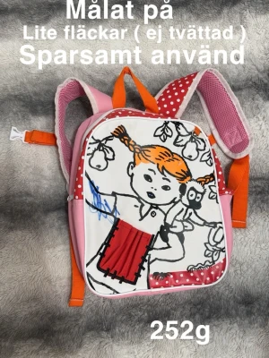 Pippi Långstrump rosa ryggsäck - Säljer en färgglad ryggsäck med Pippi Långstrump-motiv. Väskan är rosa med orange detaljer och har vita prickar på röd bakgrund på axelremmar och framsida. Insidan är orange med ett randigt fack. Materialet är bomull och polyester, och väskan har dragkedja.🌸En sån väska man målar på. Lite målat. Pennor ingår ej. Ej tvättad så lite fläckar/mörkare på vissa ställen. Sparsamt använd.