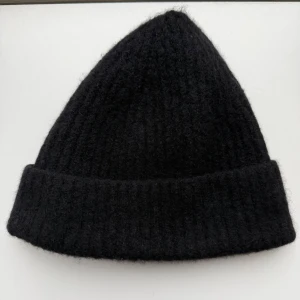 Isabel Benenato Jak/Merinoull mössa - Svart, ribbstickad mössa med uppvikt kant från Isabel Benenato. Tillverkad i en mjuk blandning av merinoull, yak, polyamid och elastan. Mycket fint skick