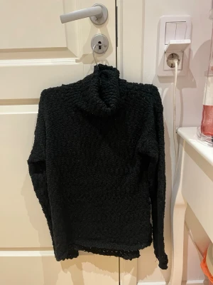 Svart polotröja från H&M - Mysig svart polotröja från H&M i fluffigt stickat material. Tröjan har lång ärm och hög polokrage som ger extra värme. Perfekt för kyliga dagar och enkel att matcha med olika outfits.