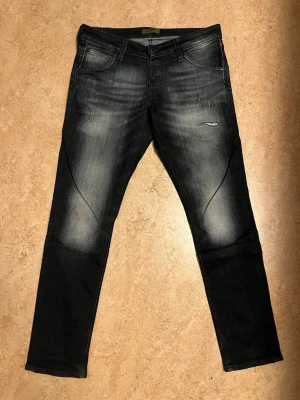 Jack & Jones Slim Glenn svarta jeans - Svarta jeans från Jack & Jones, modell Slim Glenn. Snyggt tvättade med ljusare partier och klassisk femficksdesign. Slim fit med smalare ben och normal midja. Materialet är stretchigt jeans för skön passform.