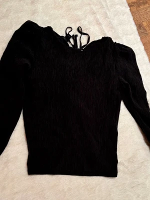 Svart långärmad blus med snörning - Säljer en svart blus från lindex i storlek L. Toppen har lång ärm, lätt puff vid axlarna och snygg snörning baktill. Materialet är ribbat och har en skön, stretchig känsla. Perfekt att styla med kjol eller jeans för en cool look.