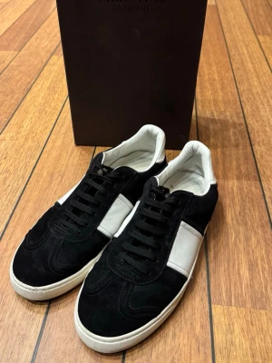 Valentino flycrew svarta - Svarta och vita sneakers från Valentino Garavani med snygga nitar på sidan av sulan. Skorna har svart snörning och är tillverkade i mocka med Vit insida. Kommer med originalkartong och dustbag.                                                                         OBS! Det saknas en nit på vardera sko.