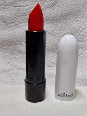 Popfeel rött läppstift LB03 - Snyggt rött läppstift från Popfeel i nyansen LB03. Hylsan är svart med vit kork och har en stilren design. Läppstiftet har en klassisk spetsig form som gör det enkelt att applicera med precision. Perfekt för dig som vill ha en djärv och färgstark look.