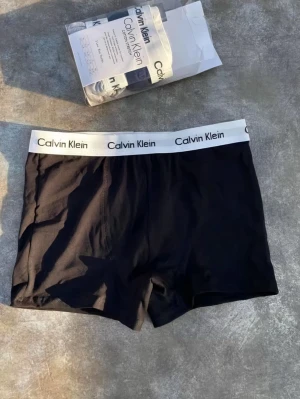 Calvin Klein boxershorts 3-pack - Säljer ett 3-pack boxershorts från Calvin Klein i klassisk modell med bred vit resår och logga. Färgerna är svart, ljusgrå och marinblå. Materialet är mjuk och stretchig bomull som sitter skönt hela dagen. Perfekt för dig som gillar stilrena underkläder.