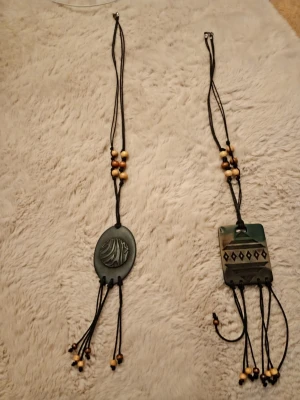 Halsband  - Bilderna visar två halsband med dekorativa hängen och träpärlor, men ingen väst finns med.