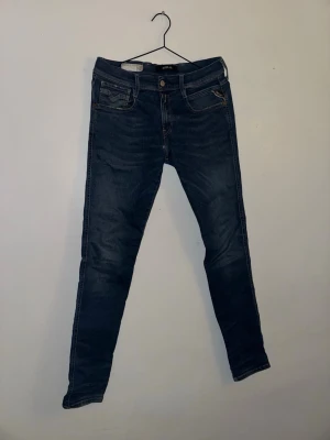 Replay mörkblå skinny jeans - Snygga mörkblå jeans från Replay med klassisk femficksdesign och smal passform. Jeansen har diskreta slitningar och kontrastsömmar, samt en liten Replay-logga på fickan. Perfekta för dig som gillar en stilren och modern look.