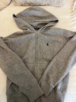Grå ralph lauren zip hoodie  - Skit snygg ralph lauren zip hoodie, det ska vara snören till hoodien ( som jag har tappat bort ). Men den är lika snygg utan snören.💖 ge gärna pris förslag❗️