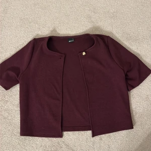 Vinröd kofta från Gina Tricot - Säljer en vinröd kofta från Gina Tricot med korta ärmar och en fin guldknapp! Superfin till middag eller skolan. Knappt använd och därav säljer jag den!