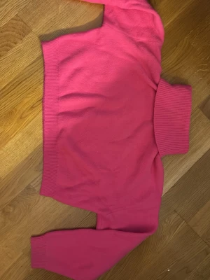 Croppad rosa polotröja - Säljer en croppad polotröja i stark rosa färg med ribbade muddar och krage. Tröjan har lång ärm och är stickad i ett mjukt material som passar perfekt för kyliga dagar. Enkel och snygg design som ger en cool vibe till din outfit. Tröjan är i storlek L men funkar även för M och S