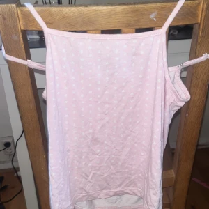 Ljusrosa linnetopp med hjärtan - Söt ljusrosa linnetopp från 157 med vita små hjärtan som mönster. Toppen har smala axelband och ärmlös design, perfekt för varma dagar. Materialet känns mjukt och lätt, troligen bomull. Enkel och gullig stil som passar dig som gillar pastell och söta detaljer.