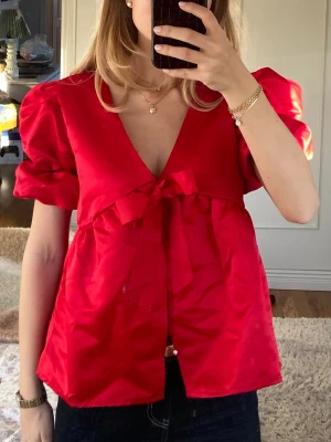 Röd blus med rosett och puffärmar - Säljer denna superfina då jag bara fått användning en gång för den. Är i jättefint skick. Slutsåld på hemsidan. Sista bilden är lånad ❣️