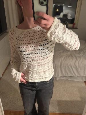 Vit stickad långärmad tröja - Säljer en vit stickad tröja med lång ärm och snyggt hålmönster. Tröjan har rund hals och är lite loose i passformen, perfekt att styla med jeans eller kjol. Materialet är mjukt och luftigt, vilket gör den skön att bära under vår och sommar.