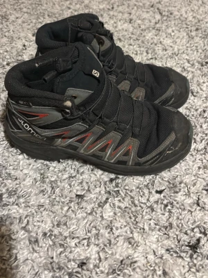 Salomon XA Pro svarta sneakers - Salomon XA Pro sneakers i svart med grå och röda detaljer. Skorna har robust snörning och slitstark sula med grovt mönster för extra grepp. Ovandelen är tillverkad i syntet och mesh, perfekt för dig som gillar äventyr och outdoor.