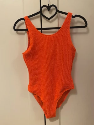 Orange ribbad baddräkt storlek 158/164 - Säljer en orange baddräckt för barn i storlekarna 158/164. Modellen har breda axelband och en djupare urringning i ryggen. Materialet är stretchigt och känns skönt mot huden.💕