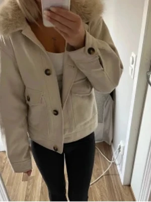 Beige jacka med pälskrage  - Säljer en beige jacka från H&M med stor, fluffig päls-krage. Jackan har stora knappar framtill, två fickor med lock och en rak. Perfekt för dig som vill ha en snygg och trendig look i höst och vinter. Inte använd så många gånger  (LÅNADE BILDER)