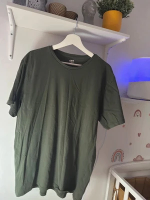 Olivgrön t-shirt från 157 - Säljer en enkel olivgrön t-shirt från 157 med rund hals och korta ärmar. T-shirten har en loose passform och är tillverkad i mjuk bomull, perfekt för chill dagar. Färgen är snyggt mörkgrön och passar till det mesta. Hängs på galge, redo att flytta in i din garderob.