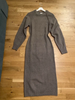 Gråbrun stickad långklänning - Mysig grå stickad långklänning med rund hals och långa ärmar. Klänningen har en enkel och stilren design som passar perfekt för kyliga dagar, passform är åsittande. 