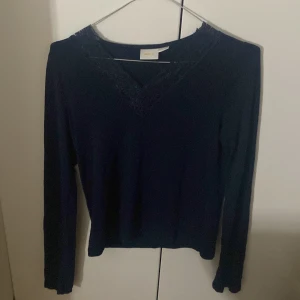 Mörkblå långärmad topp från Gina Tricot - Snygg mörkblå långärmad topp från Gina Tricot med v-ringad hals och spetsdetaljer runt ringningen. Perfekt för dig som gillar stilrena plagg med en liten twist. Mjuk och skön kvalitet som sitter bra på kroppen.
