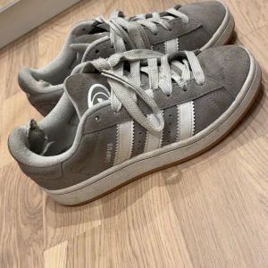Grå Adidas Campus sneakers strl 36⅔ - Säljer ett par Adidas Campus Storlek 36 2/3 Klassiska grå/vita Campus – supersnygga och passar till allt! Använda en del, lite slitage på insidan av hälen (syns på bilden) men annars i bra skick och fortfarande sköna att gå i, orginalpris 1200kr