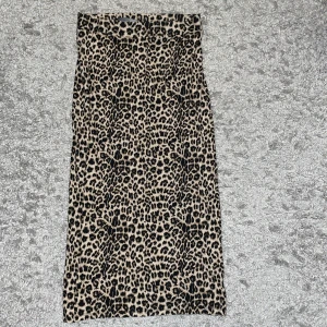 Leopardmönstrad långkjol XS - Snygg långkjol från Black Label Collection i leopardmönster. Kjolen har en rak och smal passform och är gjord i mjukt syntetmaterial med beige och svarta toner. Perfekt för dig som vill sticka ut med ett djuriskt print.