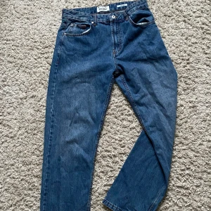 Blå wide leg jeans från Pull&Bear - Säljer ett par blå jeans från Pull&Bear med wide leg-passform. Klassisk femficksmodell med knapp och dragkedja framtill. Jeansen har en snygg mörkblå tvätt och är tillverkade i jeansmaterial med kontrastsömmar.