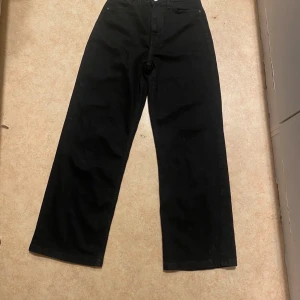 Svarta wide jeans med hög midja - Säljer ett par svarta jeans med hög midja och raka, vida ben. Klassisk femficksmodell i mjukt jeanstyg, perfekta för en avslappnad och trendig look. Passar dig som gillar stilrena och enkla byxor med lite extra utrymme i benen.
