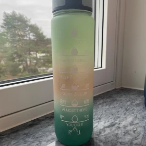 Vattenflaska med tidsmarkeringar - Motiverande vattenflaska i gradientfärg med tidsmarkeringar och peppande texter. Praktisk flip-lock-kork för enkel användning. Flaskan är i gott skick, endast mindre slitage på texten vid 'REFILL'. Perfekt för att hålla koll på vätskeintaget hela dagen.