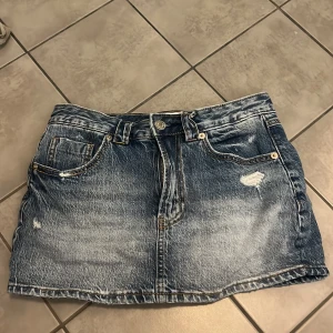 Blå jeanskjol med slitningar shorts i den så ingen kan se underkläderna - Snygg blå jeanskjol från stradivarius med klassisk femficksdesign och slitna detaljer framtill. Kjolen har bälteshällor, knapp och dragkedja i midjan samt två stora bakfickor. Perfekt för dig som gillar en avslappnad och trendig denimlook. Shorts i den så ingen kan så underkläderna