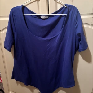 Blå kortärmad body med rund hals - Snygg blå body med rundad halsringning och korta ärmar. Enkel och stilren design som passar perfekt till jeans eller kjol. Mjuk och skön känsla, troligtvis i bomull. Perfekt för dig som gillar basic men ändå vill sticka ut med färg.