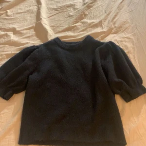 Svart stickad tröja med puffärm - Mysig svart stickad tröja med puffiga ärmar och rund halsringning. Tröjan har ribbade muddar vid ärmslut. Bara testad aldrig använd!
