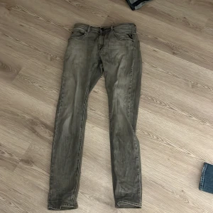 Replay grå jeans slim fit - Snygga grå jeans från Replay med slim fit och klassisk femficksdesign. Jeansen har en lätt tvättad look och detaljerade sömmar på bakfickorna. Passar dig som gillar en smal siluett och vill ha ett stilrent plagg i garderoben.